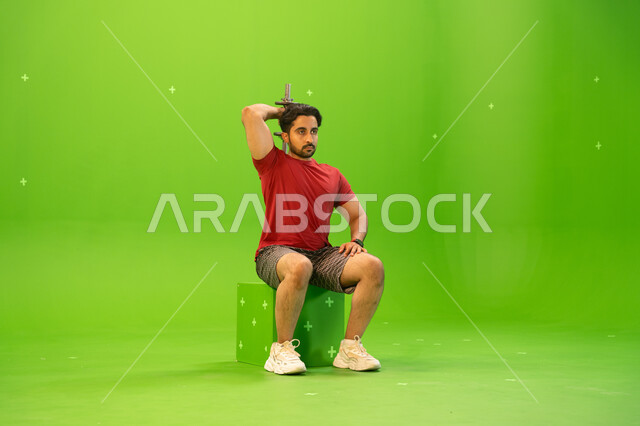 رفع الأوزان الحديدية الثقيلة، تقوية عضلات الجسم وبناؤها، تمارين رفع الأثقال، القوة والتحدي والتحفيز لأسلوب حياة صحي، بورتريه لشاب عربي خليجي سعودي يمارس التمارين الرياضية مع الدمبلز، نشاط بدني للمحافظة على الصحة واللياقة الجسدية، خلفية خضراء، كروما.