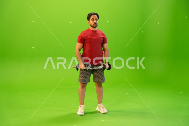 كمال الأجسام وتقوية وبناء العضلات، تمارين رفع الأثقال، أسلوب حياة صحي، بورتريه لشاب عربي خليجي سعودي يمارس التمارين الرياضية مع الدمبلز، نشاط بدني للمحافظة على الصحة واللياقة الجسدية، رفع الأوزان الحديدية الثقيلة، خلفية خضراء، كروما.