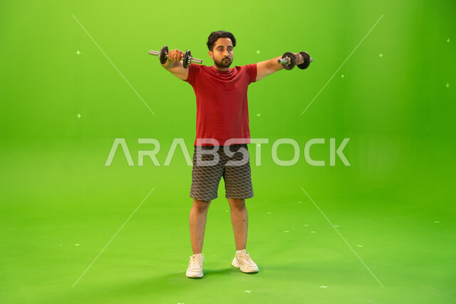 كمال الأجسام وتقوية وبناء العضلات، تمارين رفع الأثقال، أسلوب حياة صحي، بورتريه لشاب عربي خليجي سعودي يمارس التمارين الرياضية مع الدمبلز، نشاط بدني للمحافظة على الصحة واللياقة الجسدية، رفع الأوزان الحديدية الثقيلة، خلفية خضراء، كروما.