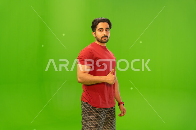 الوقوف بثقة والنظر إلى الكاميرا، بورتريه مقرب لرجل عربي سعودي خليجي يشير بيده بعلامة الموافقة, إيماءات يدين وحركات تدل على الاعجاب والقبول, مفهوم لغة الجسد، خلفية خضراء، كروما.