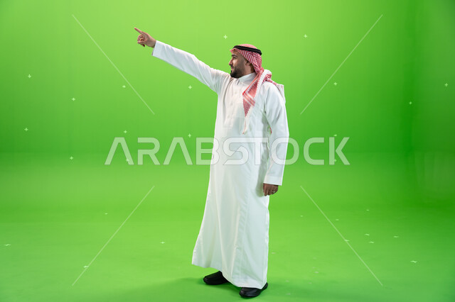 Pointing with the index finger at something, full-length body image, standing upright, concept of body language, movements and gestures, portrait of a Saudi Arabian Gulf man wearing the traditional Saudi shemagh and thobe, green background, chrome.
