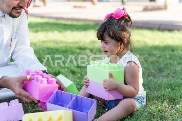 A beautiful girl with Down syndrome spends her time outing with her father in the park, a Saudi Gulf father plays with his daughter outdoors, people of determination, people with special needs