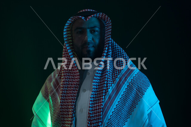 مفهوم الشياكه والاهتمام بالمظهر الخارجي، شاب وسيم ينظر الى الكاميرا ،شخصيه سعوديه بارزه ،ايماءات الثقه بالنفس والاعتزاز، بورتريه مقرب لرجل عربي خليجي سعودي مبتسم يرتدي الثوب والشماغ التقليدي يقف باستقامة، خلفية سوداء مع إضاءة ملونه