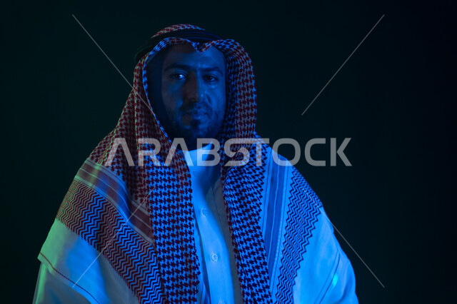 شاب وسيم ينظر الى الكاميرا ،شخصيه سعوديه بارزه ،ايماءات الثقه بالنفس والاعتزاز، بورتريه مقرب لرجل عربي خليجي سعودي مبتسم يرتدي الثوب والشماغ التقليدي يقف باستقامة، مفهوم الشياكه والاهتمام بالمظهر الخارجي، خلفية سوداء مع إضاءة ملونه