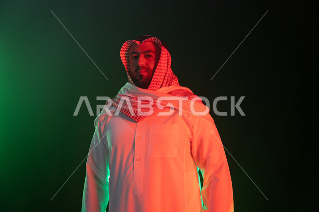 شخصيه مهمة بارزه سعودية ،ايماءات الثقه بالنفس والاعتزاز، بورتريه مقرب لرجل عربي خليجي سعودي مبتسم يرتدي الثوب والشماغ التقليدي يقف باستقامة، النظر إلى الكاميرا، مفهوم الشياكه والاهتمام بالمظهر الخارجي، خلفية سوداء مع إضاءة ملونه