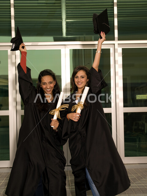 إيماءات وجه تدل على السعادة والفرح والفخر, التعليم في جامعات الامارات العربية، الاحتفال بالتخرج من الجامعة برفع القبعة عاليا، صورة مقربة لخريجتين جامعيتين عربيتين خليجيتين اماراتيتين ترتديان ملابس التخرج وتمسكان شهادة النجاح