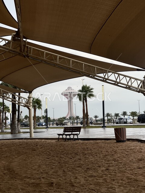 النمو والتطور العمراني في السعودية، الفن الهندسي المعماري لبرج المياه في مدينة الخبر، أشجار النخيل الخضراء على كورنيش الخبر، كرسي خشبي تحت مظلة جلوس في أحد الأماكن العامة، معالم الخبر المشهورة، أماكن سياحية مشهورة