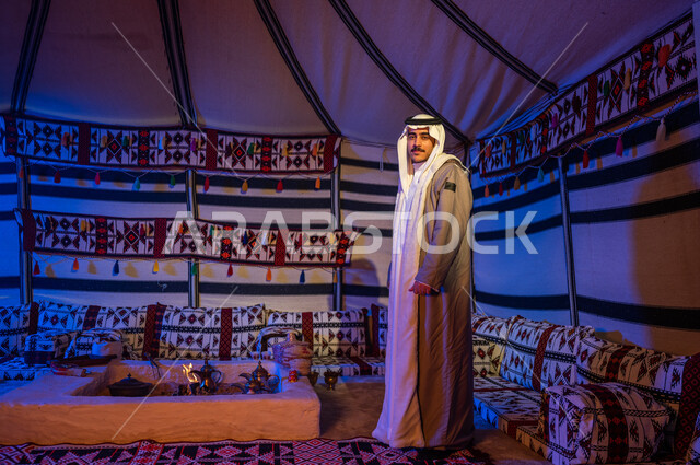 الأجواء الهادئة في أماكن التخييم، إيماءات وجه تدل على السرور، رحلة وكشتة بر في الأجواء الشتوية في الصحراء، خيمة بدوية شعبية تراثية في السعودية، رجل عربي خليجي سعودي مبتسم يرتدي الفروة والغترة يقف داخل بيت شعر ينظر إلى الكاميرا، صورة الجسم بالطول الكامل