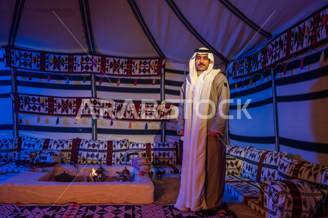 الأجواء الهادئة في أماكن التخييم، إيماءات وجه تدل على السرور، رحلة وكشتة بر في الأجواء الشتوية في الصحراء، خيمة بدوية شعبية تراثية في السعودية، رجل عربي خليجي سعودي مبتسم يرتدي الفروة والغترة يقف داخل بيت شعر ينظر إلى الكاميرا، صورة الجسم بالطول الكامل
