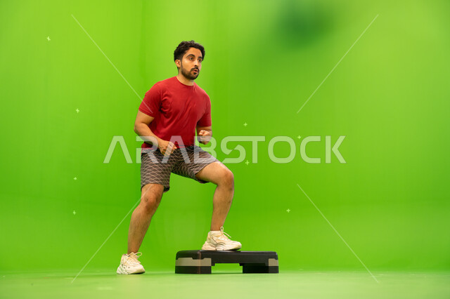 تمارين زيادة نبضات القلب، بورتريه لشاب عربي خليجي سعودي يرتدي الملابس الرياضية و يقوم في ممارسة تمارين الايبروبيكس التدريجيه ،المحافظة على اللياقة الجسدية، أنشطة ورياضات شبابية ترفيهية ,صحة ورشاقه، صورة الجسم بالطول الكامل ،خلفية خضراء ،كروما