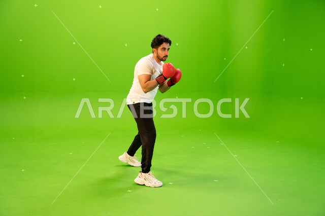 المنتخب الوطني السعودي للملاكمة والمصارعة، التدرب على حركات قتالية، ملاكم عربي خليجي سعودي يرتدي قفازات الملاكمة يمارس رياضة الدفاع عن النفس، نشاط بدني للحفاظ على الصحة واللياقة الجسدية، صورة الجسم بالطول الكامل، خلفية خضراء ،كروما