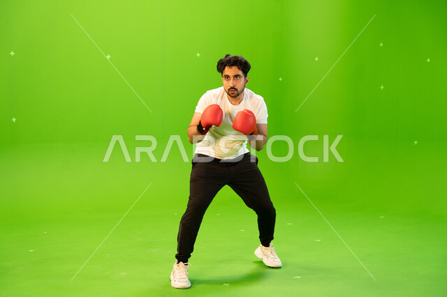 المنتخب الوطني السعودي للملاكمة والمصارعة، التدرب على حركات قتالية، ملاكم عربي خليجي سعودي يرتدي قفازات الملاكمة يمارس رياضة الدفاع عن النفس، نشاط بدني للحفاظ على الصحة واللياقة الجسدية، صورة الجسم بالطول الكامل، خلفية خضراء ،كروما