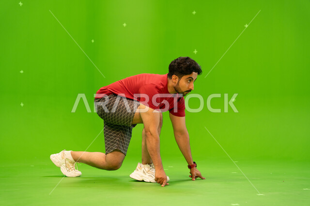 ممارسة هواية الركض والجري، الاهتمام باللياقه الجسديه والبدنيه، بورتريه لرجل عربي خليجي سعودي يرتدي الزي الرياضي يأخذ وضعيه الاستعداد لبدء السباق، انشطة ورياضات ترفيهيه شبابيه للمحافظة على الصحه ،  خلفية خضراء ، كروما