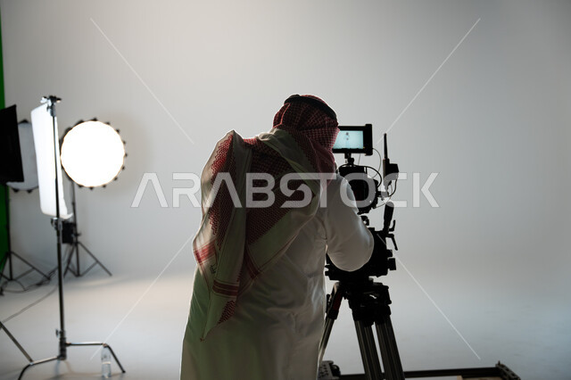 ممارسة هواية التقاط الصور بكاميرات عالية الدقة, موهبة واحتراف التصوير الفوتوغرافي, رجل عربي خليجي سعودي يرتدي الثوب التقليدي والشماغ يمسك كاميرا التصوير, أخذ صور تذكارية, خلفية استديو