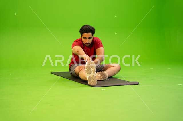 شد عضلات البطن، بورتريه لشاب عربي خليجي سعودي يرتدي الملابس الرياضية و يقوم في ممارسة التمارين الرياضية للمحافظة على اللياقة الجسدية، الصحة والرشاقه، أنشطة ورياضات شبابية ترفيهية في المملكة العربية السعودية، خلفية خضراء ، كروما