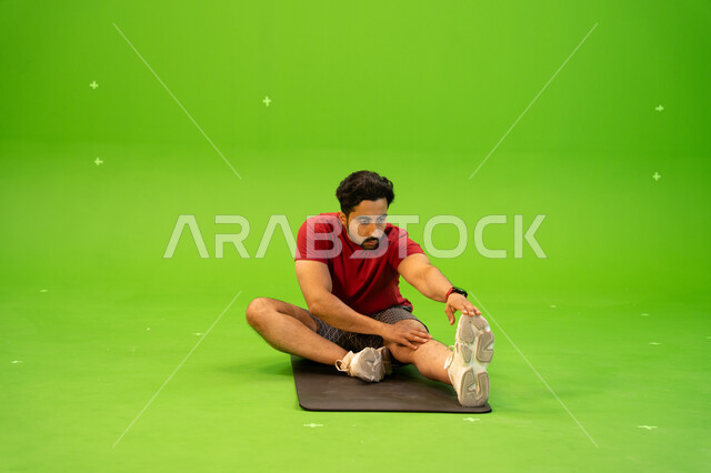 شد عضلات البطن، بورتريه لشاب عربي خليجي سعودي يرتدي الملابس الرياضية و يقوم في ممارسة التمارين الرياضية للمحافظة على اللياقة الجسدية، الصحة والرشاقه، أنشطة ورياضات شبابية ترفيهية في المملكة العربية السعودية، خلفية خضراء ، كروما