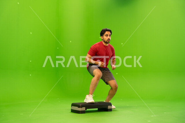 تمارين زيادة نبضات القلب، بورتريه لشاب عربي خليجي سعودي يرتدي الملابس الرياضية و يقوم في ممارسة تمارين الايبروبيكس التدريجيه ،المحافظة على اللياقة الجسدية، أنشطة ورياضات شبابية ترفيهية ,صحة ورشاقه، صورة الجسم بالطول الكامل ،خلفية خضراء ،كروما