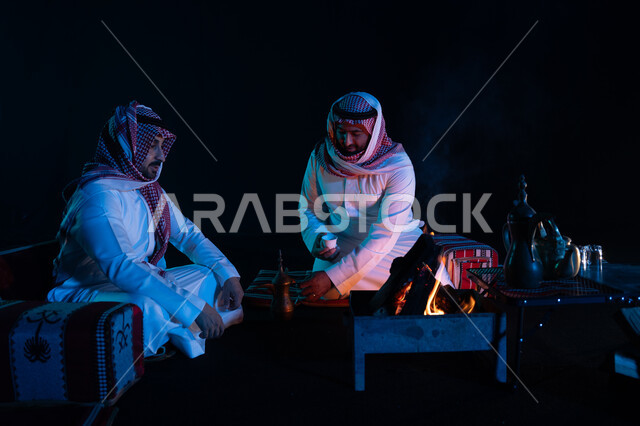 حسن الضيافة والاستقبال, تقديم القهوة العربية للضيوف، الجلسات السعودية التقليدية الشعبية، قضاء أوقات ممتعة في الأجواء الليلية في الصحراء السعودية, رجلان عربيان خليجيان سعوديان يرتديان الشماغ والزي التقليدي في رحلة تخييم برية، كشتة بر شبابية مسائية