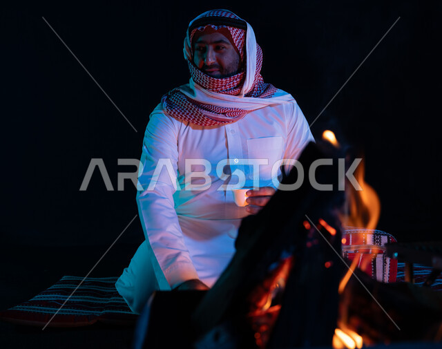 الجلسات السعودية التقليدية الشعبية، الاستمتاع بشرب القهوة العربية, قضاء أوقات ممتعة في الأجواء الليلية, رجل عربي خليجي سعودي يرتدي الشماغ والزي التقليدي في رحلة تخييم برية، صورة مقربة لشعلة حطب في الصحراء السعودية، كشتة بر شبابية مسائية