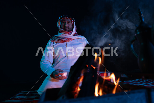 الجلسات السعودية التقليدية الشعبية، الاستمتاع بشرب القهوة العربية, قضاء أوقات ممتعة في الأجواء الليلية, رجل عربي خليجي سعودي يرتدي الشماغ والزي التقليدي في رحلة تخييم برية، صورة مقربة لشعلة حطب في الصحراء السعودية، كشتة بر شبابية مسائية
