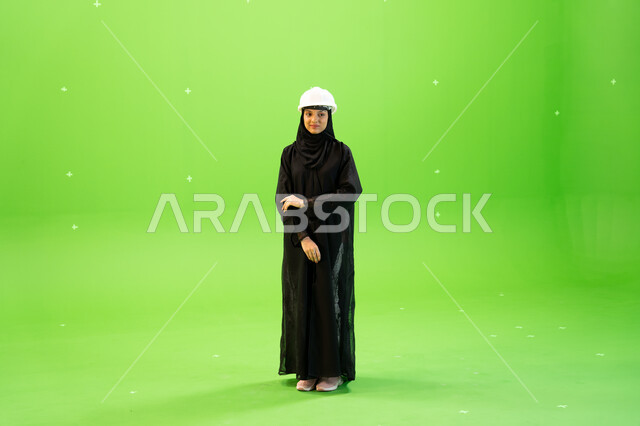 وظائف ومهن هندسية، مهندسات المملكة العربية السعودية, إدارة ودراسة المشاريع الهندسية، بورتريه لمهندسة عربية خليجية سعودية محجبة ترتدي العباءة السوداء و خوذة الحماية بإيمات تدل على الثقة، صورة الجسم بالطول الكامل, كروما، خلفية خضراء