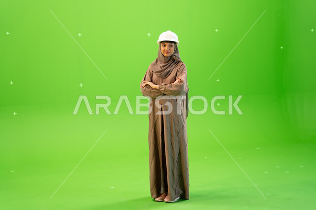 التواجد في موقع العمل, مهندسات المملكة العربية السعودية, بورتريه لمهندسة عربية خليجية سعودية محجبة ترتدي العباءة و خوذة الحماية تنظلر الى الكاميرا بإيمات تدل على الثقة، الوقوف بأيدي متقاطعة، صورة الجسم بالطول الكامل, كروما، خلفية خضراء