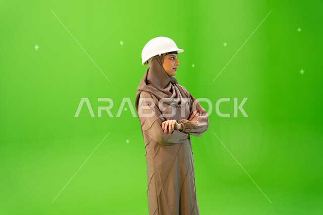 مهندسات المملكة العربية السعودية, إدارة ودراسة المشاريع الهندسية، بورتريه من الجانب لمهندسة عربية خليجية سعودية محجبة ترتدي العباءة و خوذة الحماية بإيمات تدل على الثقة، الوقوف بأيدي متقاطعة، كروما، خلفية خضراء