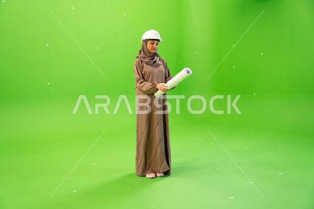 التدقيق والإشراف على العمل، التحقق من تنفيذ المشاريع الإنشائية , مفهوم الهندسة والإنشاءات المعمارية، بورتريه لمهندسة عربية خليجية سعودية محجبة و خوذة الحماية وتمسك بيدها مخططات وتصاميم هندسية، صورة الجسم بالطول الكامل, كروما، خلفية خضراء