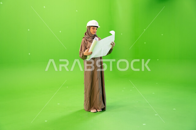 مفهوم الهندسة والإنشاءات المعمارية، التحقق من تنفيذ المشاريع الإنشائية , بورتريه لمهندسة عربية خليجية سعودية محجبة و خوذة الحماية وتمسك بيدها مخططات وتصاميم هندسية، التدقيق والإشراف على العمل، صورة الجسم بالطول الكامل, كروما، خلفية خضراء