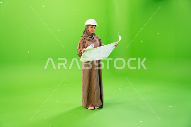 مفهوم الهندسة والإنشاءات المعمارية، التحقق من تنفيذ المشاريع الإنشائية , بورتريه لمهندسة عربية خليجية سعودية محجبة و خوذة الحماية وتمسك بيدها مخططات وتصاميم هندسية، التدقيق والإشراف على العمل، صورة الجسم بالطول الكامل, كروما، خلفية خضراء
