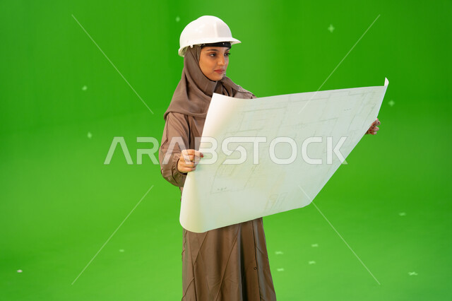 مهن ووظائف سعودية, التحقق من تنفيذ المشاريع الإنشائية , مفهوم الهندسة والإنشاءات المعمارية، بورتريه من الجانب لمهندسة عربية خليجية سعودية محجبة ترتدي العباءة السعودية و خوذة الحماية وتمسك بيدها مخططات هندسية، الإشراف على العمل، كروما، خلفية خضراء