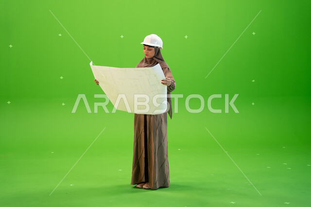 التحقق من تنفيذ المشاريع الإنشائية , مفهوم الهندسة والإنشاءات المعمارية، بورتريه لمهندسة عربية خليجية سعودية محجبة و خوذة الحماية وتمسك بيدها مخططات وتصاميم هندسية، التدقيق والإشراف على العمل، صورة الجسم بالطول الكامل, كروما، خلفية خضراء