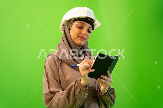 إدارة ودراسة المشاريع الهندسية، متابعة سير المشروع في موقع العمل, بورتريه مقرب لمهندسة عربية خليجية سعودية محترفة ترتدي العباءة السعودية و خوذة الحماية وتقوم بكتابة وتدوين الملاحظات، الإشراف على العمل وتدقيقه، خلفية خضراء, كروما