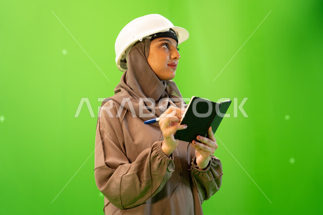 Supervising and auditing the work, following up on the progress of the project at the work site, a close-up portrait from the side of a professional Saudi Arabian Gulf engineer wearing the Saudi abaya and a protective helmet and writing and taking notes,