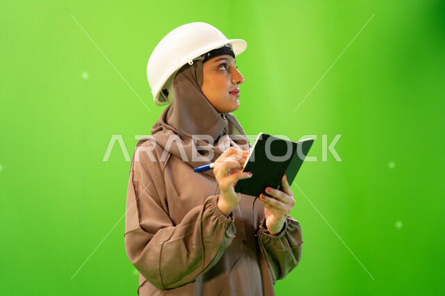 الإشراف على العمل وتدقيقه، متابعة سير المشروع في موقع العمل, بورتريه مقرب من الجانب لمهندسة عربية خليجية سعودية محترفة ترتدي العباءة السعودية و خوذة الحماية وتقوم بكتابة وتدوين الملاحظات، إدارة ودراسة المشاريع الهندسية، خلفية خضراء, كروما