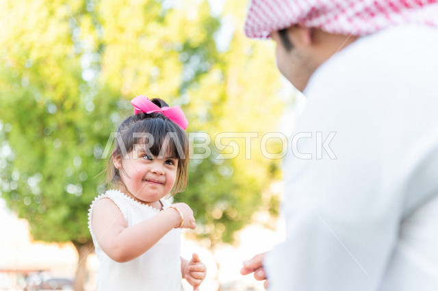 فتاه جميلة مصابة بملازمة داون تقضي وقتها في نزهه مع والدها بالمنتزه ، اب سعودي خليجي يلعب مع ابنته في الهواء الطلق ، أصحاب الهمم ، ذوي الاحتياجات الخاصة