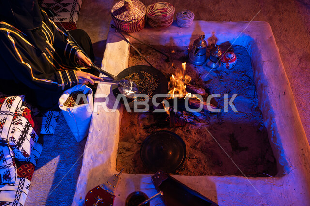 تحميص حبوب البن في المحماس على شعلة النار، داخل خيمة شعبيه تراثية، أسلوب الحياة القديمه في الباديه، إمرأة عربية خليجيه سعودية ترتدي العباءة والبرقع تقوم باستخدام المعاميل لتحضير القهوة بالطريقة التقليدية على الحطب في موقد طيني، منتج محلي ومحاصيل زراعية وطنية