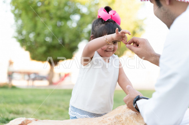 فتاه جميلة مصابة بملازمة داون تقضي وقتها في نزهه مع والدها بالمنتزه ، اب سعودي خليجي يلعب مع ابنته في الهواء الطلق ، أصحاب الهمم ، ذوي الاحتياجات الخاصة