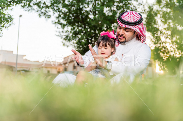 فتاه جميلة مصابة بملازمة داون تقضي وقتها في نزهه مع والدها بالمنتزه ، اب سعودي خليجي يلعب مع ابنته في الهواء الطلق ، أصحاب الهمم ، ذوي الاحتياجات الخاصة