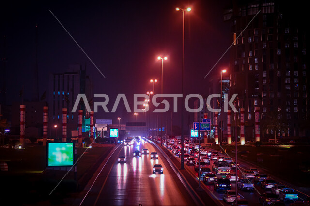 لوحات إعلانية إلكترونية على جوانب الطرق والشوارع، حركة سير السيارات على الطريق العام في مدينة الرياض، أعمدة الإنارة المضيئة في الليل، وسائل النقل والمواصلات في المملكة العربية السعودية 