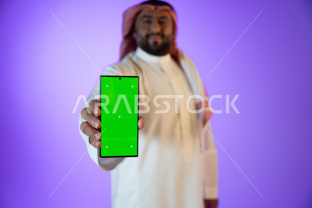 التسوق والشراء عن بعد, بورتريه لرجل أعمال عربي سعودي خليجي مبتسم يستخدام هاتفه المحمول بخلفية خضراء, كروما، استخدام تقنية السمارت على الجوال, مفهوم التسويق الالكتروني, خلفية ملونة