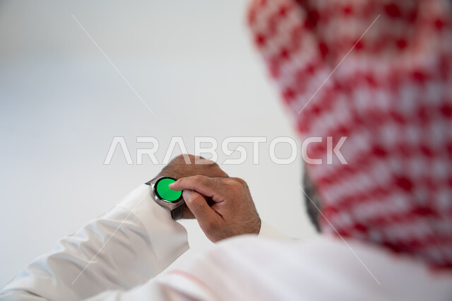 المراقبة بالتكنولوجيا عن بعد, استخدام ساعة يد الكترونية, بورتريه مقرب لرجل عربي خليجي سعودية يرتدي الثوب والشماغ التقليدي يستخدم ساعة بتقنية سمارت بخلفية خضراء, كروما, تطبيقات وبرامج التواصل الاجتماعي عبر الهاتف المحمول, خلفية بيضاء