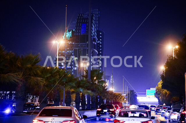 الحركة المرورية للسيارات في طرق وشوارع مدينة الرياض، الأشجار والنباتات الخضراء على جانبي الطريق، الفن الهندسي المعماري لبرج حمد المضيء ليلا، النمو والتطور العمراني في السعودية، معالم الرياض المشهورة