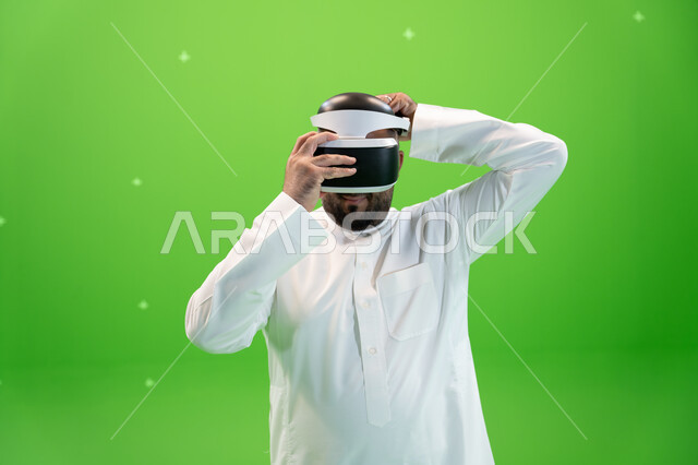 قضاء أوقات ممتعة مع ألعاب العالم الخيالي, لبس النظارات الإفتراضية ثلاثية الأبعاد، بورتريه مقرب  لرجل عربي خليجي سعودي يرتدي الزي التقليدي ويقوم بإرتداء نظارة الواقع الإفتراضي، خلفية خضراء، كروما