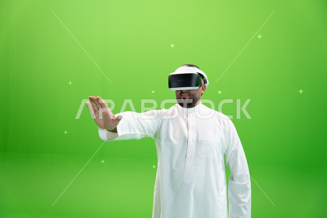 الاندماج والتفاعل مع العالم الخيالي , قضاء أوقات ممتعة مع ألعاب الواقع الافتراضي, دفع عنصر هولوجرامي، بورتريه مقرب  لرجل عربي خليجي سعودي يرتدي الزي التقليدي و نظارة الواقع الإفتراضي ثلاثية الأبعاد، خلفية خضراء، كروما