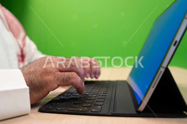 مهن ووظائف سعودية مكتبية, إجراء مقابلات عمل أونلاين, استخدام الأجهزة والتقنيات الحديثة لتسهيل الأعمال, بورتريه مقرب ليد موظف عربي سعودي خليجي يجلس في مكتبه ويستخدم التابلت بشاشة زرقاء فارغة, خلفية خضراء, كروما.