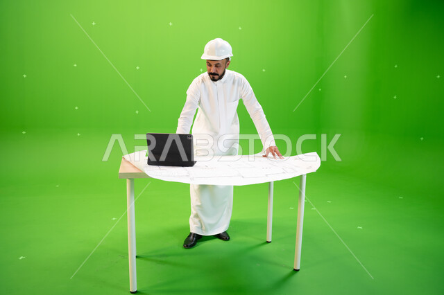 إدارة المشاريع الهندسية باستخدام الجهاز اللوحي، بورتريه لمهندس عربي خليجي سعودي يرتدي الثوب التقليدي و خوذة الحماية ويقف في موقع العمل، متابعة سير المشاريع الإعمارية, مهن ووظائف سعودية، صورة الجسم بالطول الكامل, خلفية خضراء، كروما.