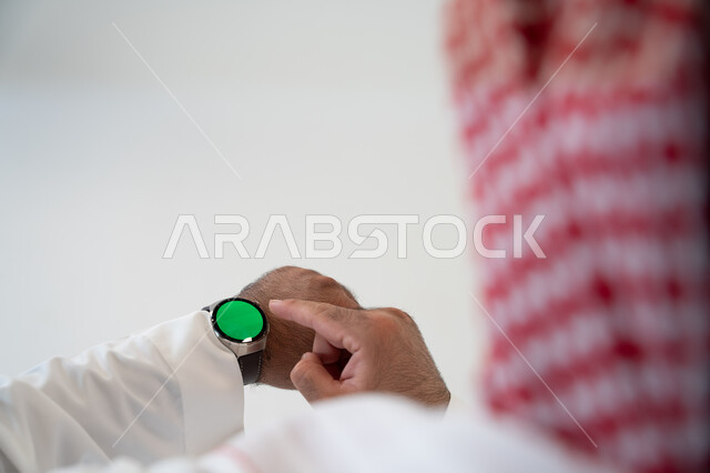 تسهيل إنجاز الأمور الشخصية باستخدام أحدث التقنيات, تتبع الإشعارات عبر الساعات الحديثة, بورتريه مقرب من الخلف لرجل عربي خليجي سعودي يرتدي الشماغ والزي التقليدي ويلبس في يده ساعة ذكية بشاشة خضراء كروما ويقوم بالنقر عليها,  خلفية بيضاء