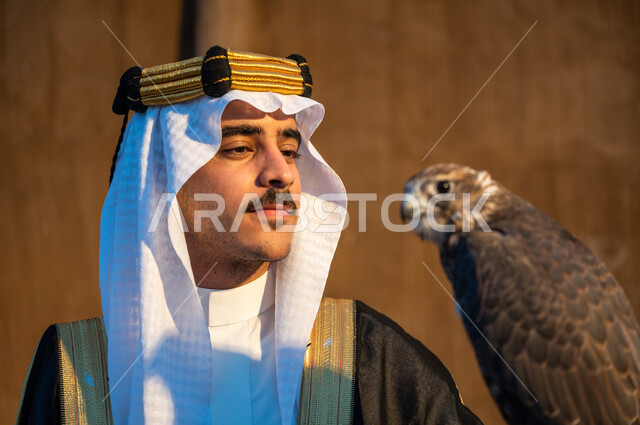 شغف السعوديين بتربية الطيور الجارحة, النظر الى الصقر بإيماءات القوة والتحدي, التمسك بموروث المملكة الحضاري والثقافي, صورة مقربة لرجل عربي خليجي سعودي يرتدي الغترة والبشت والعقال يحمل على يده طائر الصقر, علاقة الصقور تأسيس المملكة 22 فبراير, يوم التأسيس 1727