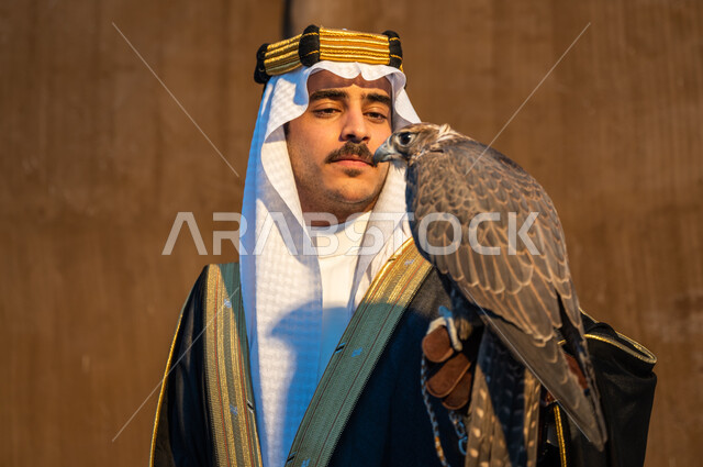 التمسك بموروث المملكة الحضاري والثقافي, صورة مقربة لرجل عربي خليجي سعودي يرتدي الغترة والبشت والعقال يحمل على يده طائر الصقر, شغف السعوديين بتربية الطيور الجارحة, علاقة الصقور تأسيس المملكة 22 فبراير, النظر الى الصقر بإيماءات القوة والتحدي, يوم التأسيس 1727